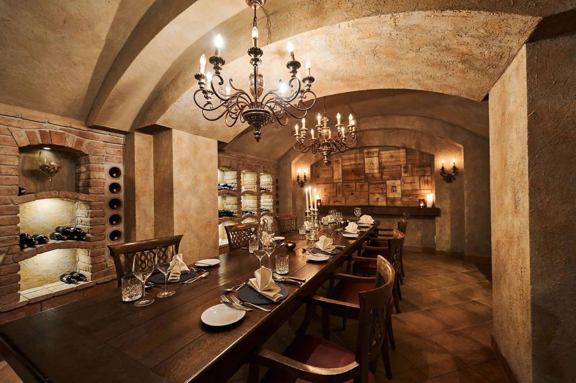 Elegant dining room in a wine cellar with a long table, plates, glasses and a chandelier.