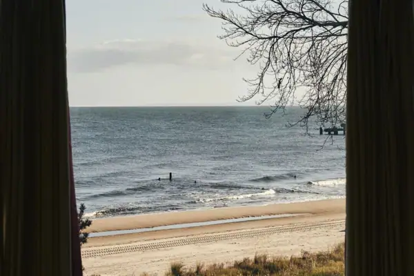 A window with curtains overlooking a beach with sand.