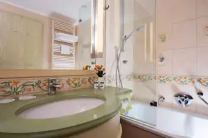 Junior double room landside with balcony Bathroom with washbasin and bathtub, tiles on the walls, tap and mirror.