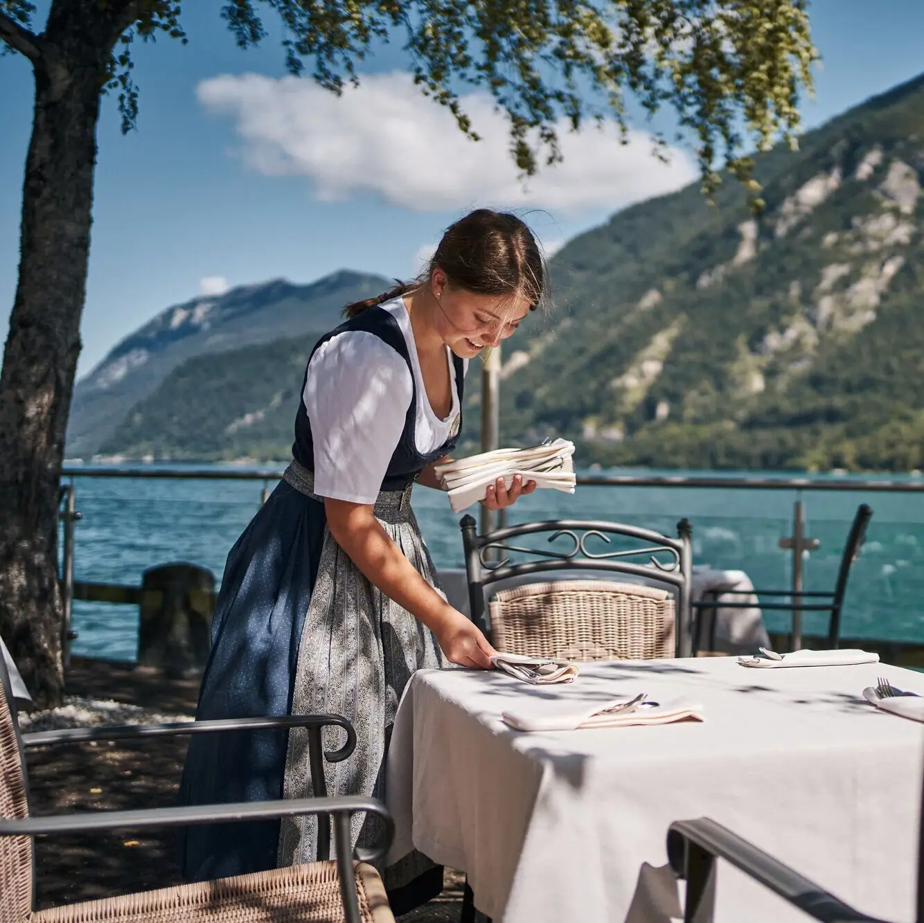 Terrace by the lake A woman in a dress at a table with a lake in the background.