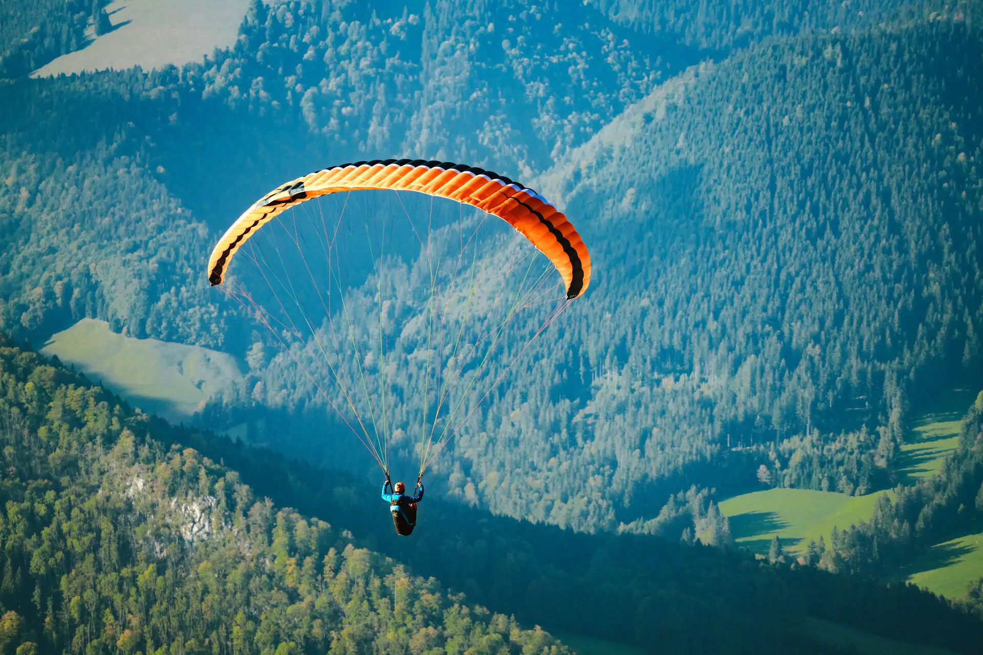 A person glides over a valley with a parachute.