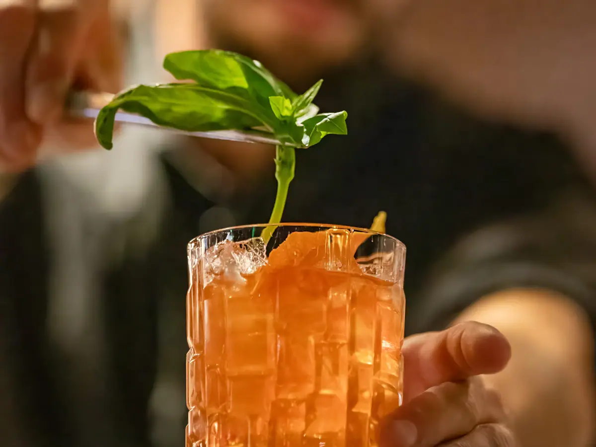 A man holds a knife over a glass with a drink.