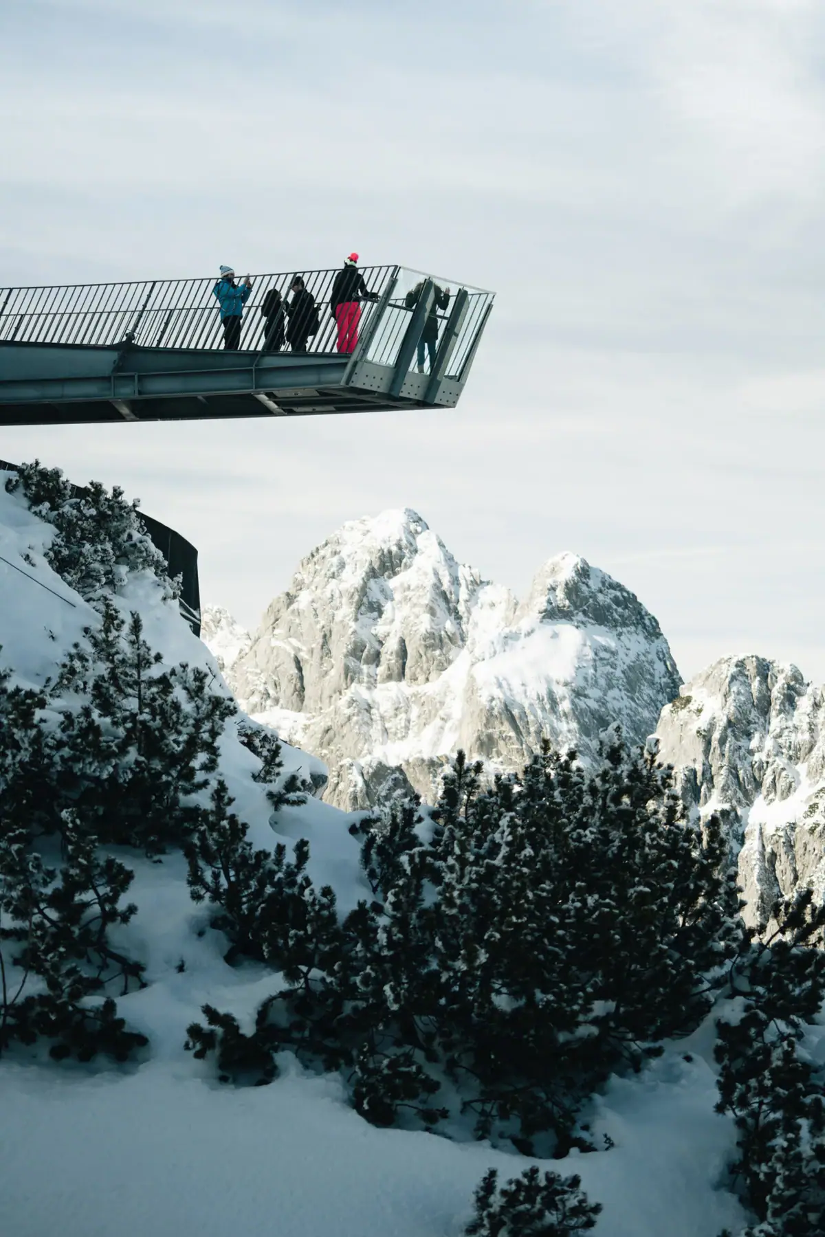 People stand on a bridge over a snow-covered mountain.