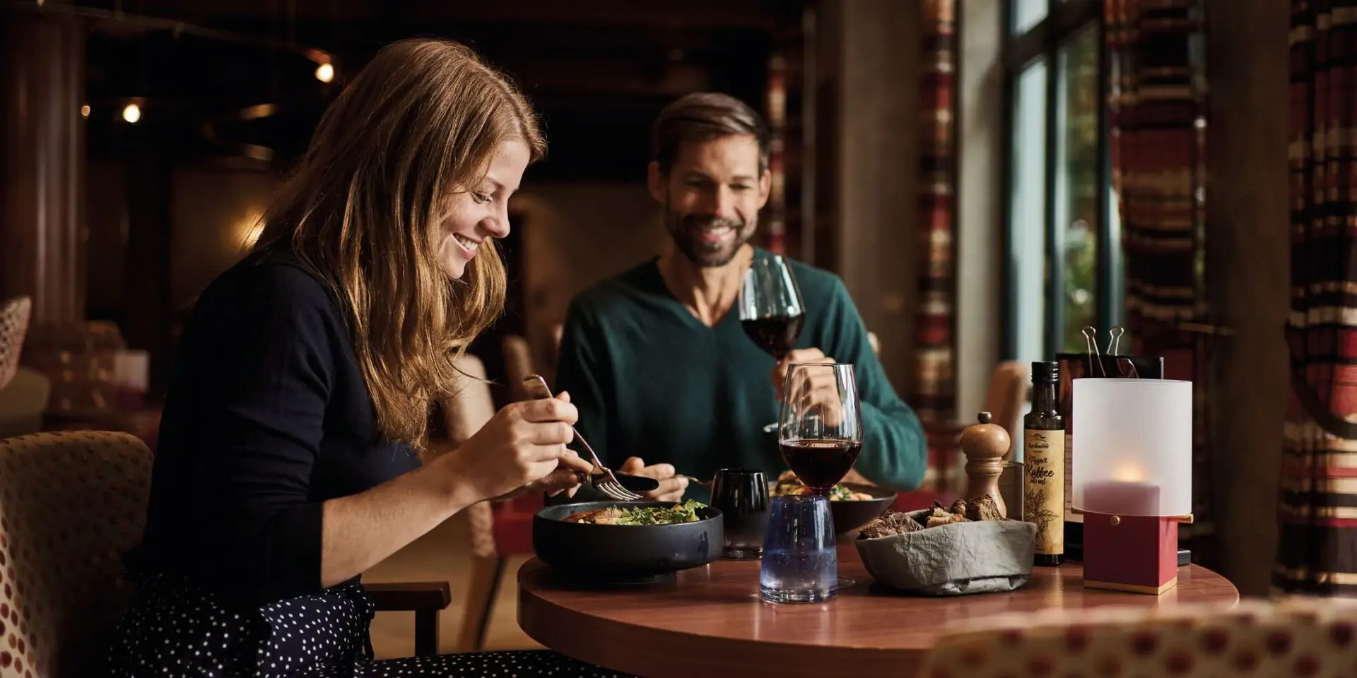 A man and a woman are sitting at a table in a restaurant with wine glasses and a bottle of wine.