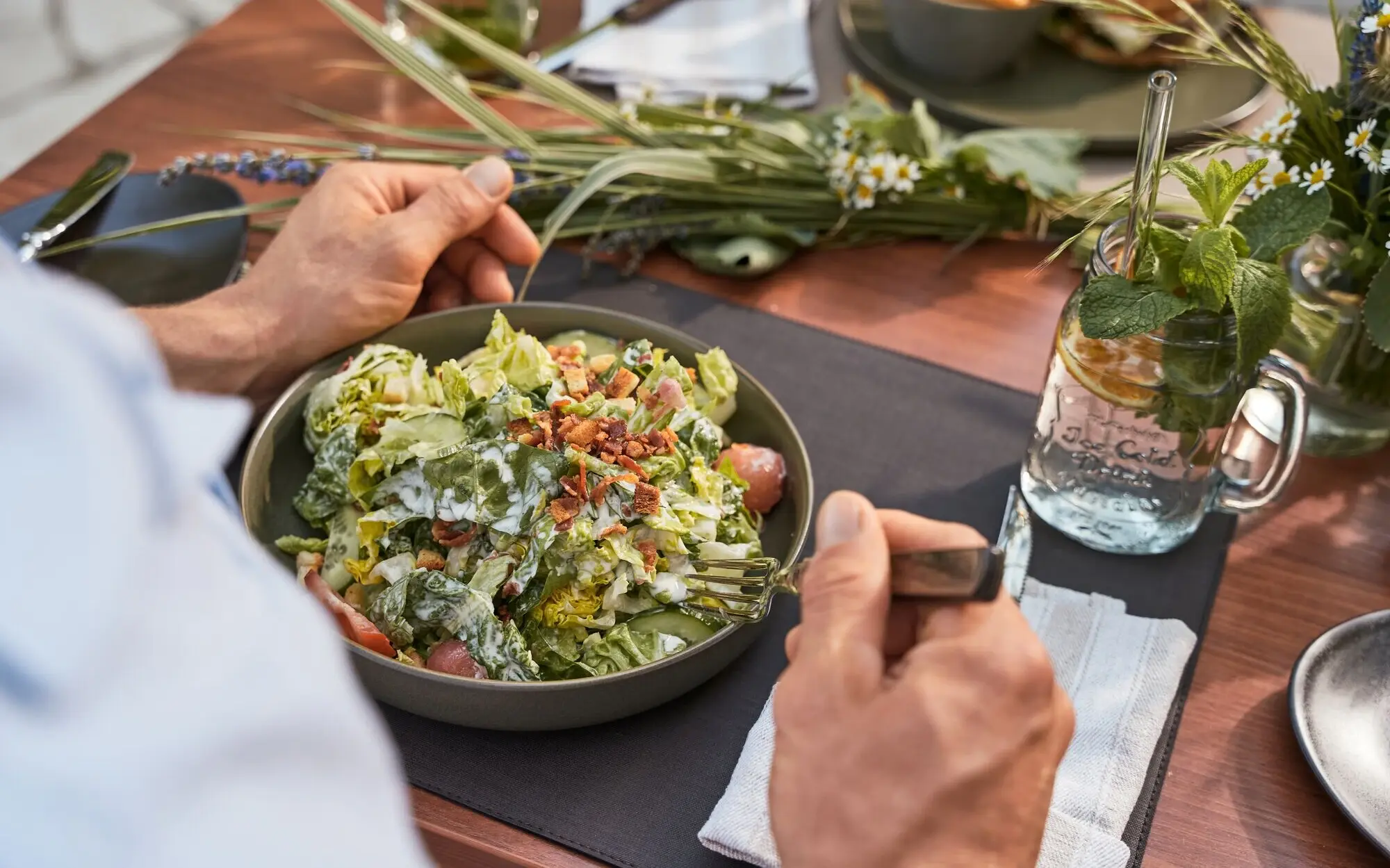 A person eats a salad at a laid table.