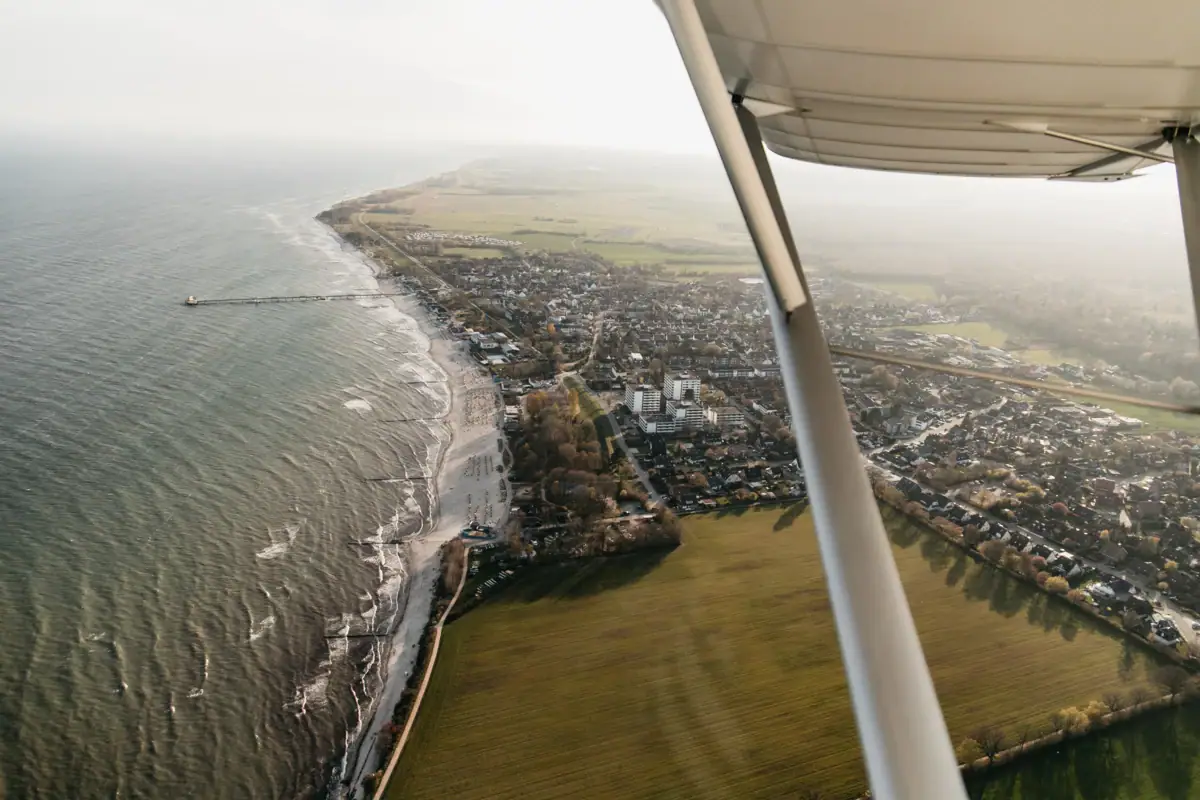 An aerial view of a beach and countryside, with water in the foreground.
