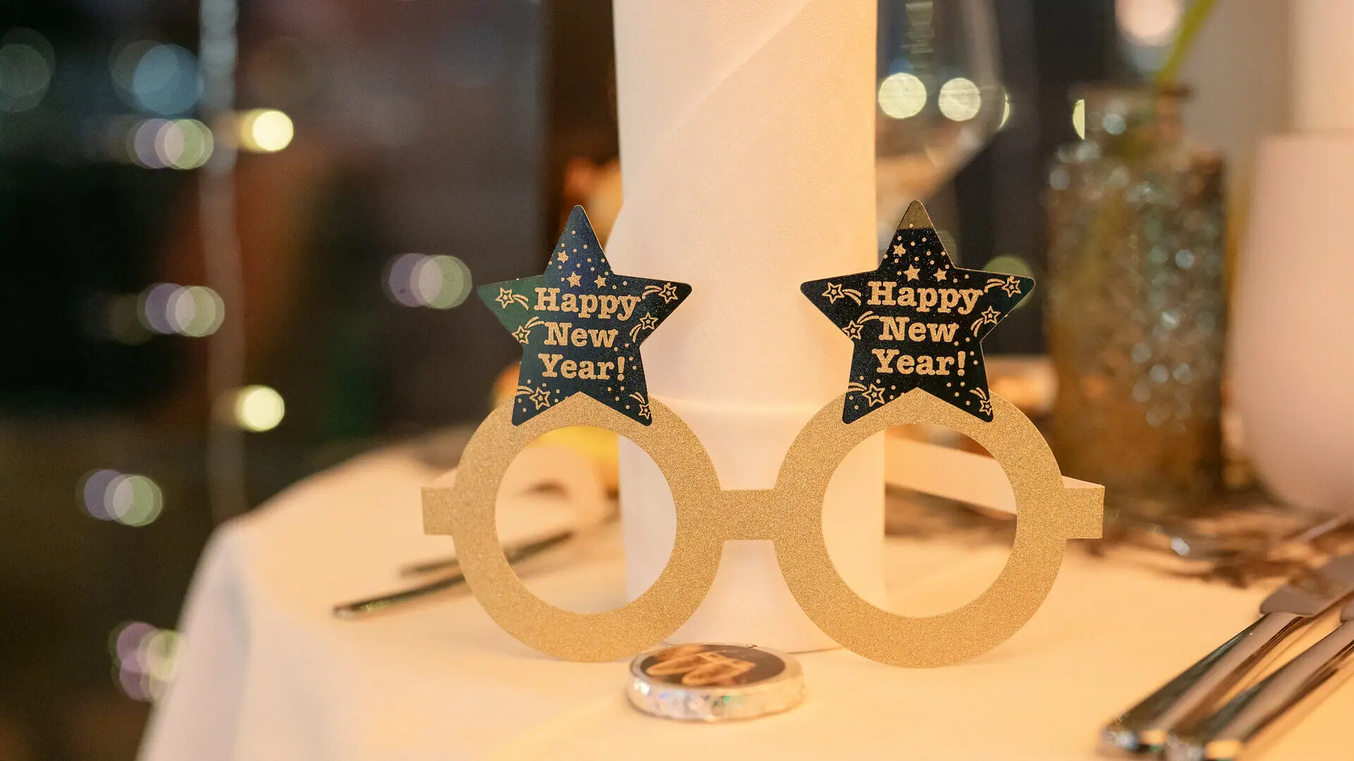 A pair of paper glasses for New Year’s Eve, with ‘Happy New Year’ written on a table.