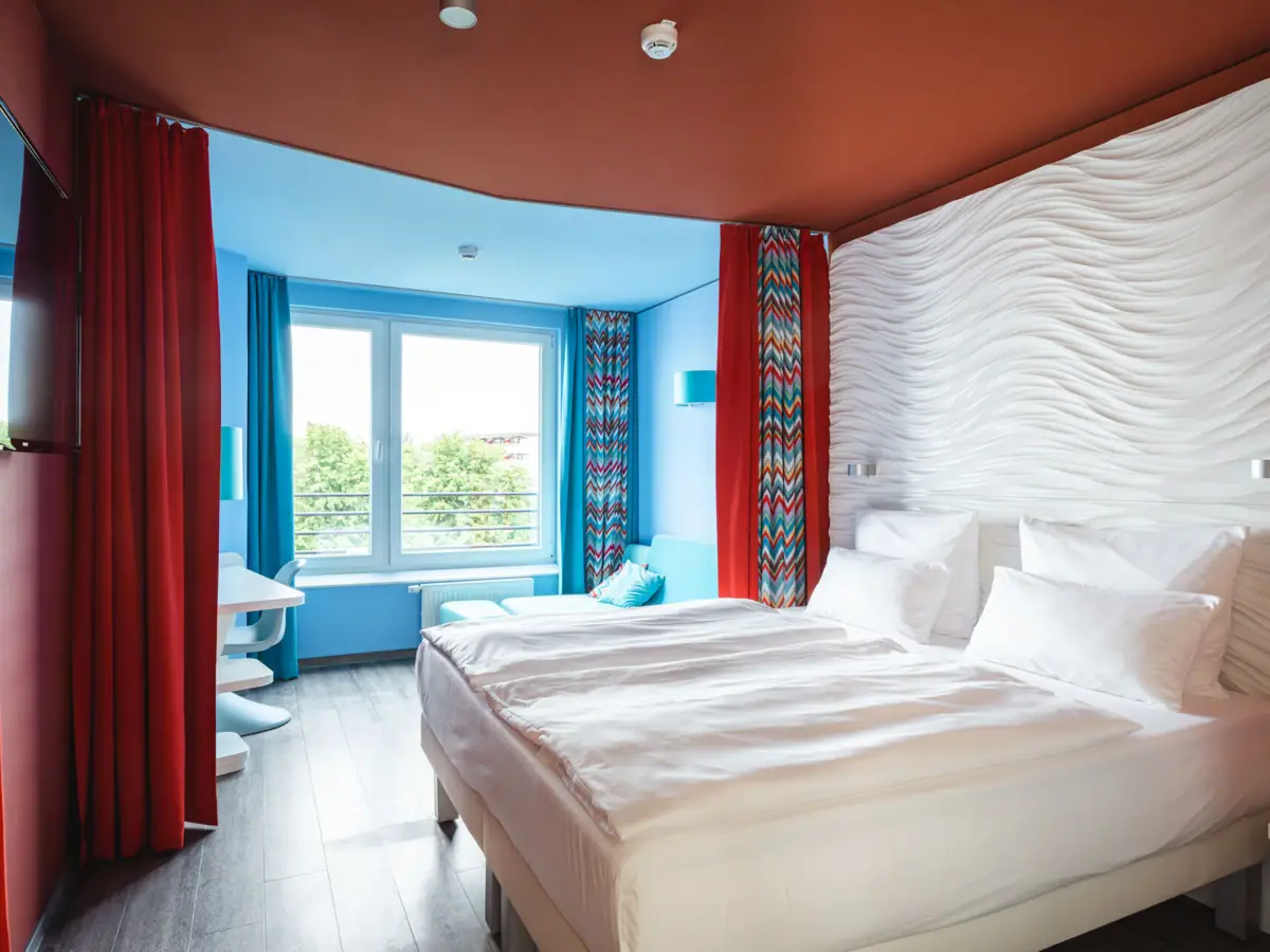 A room with two beds and red curtains.