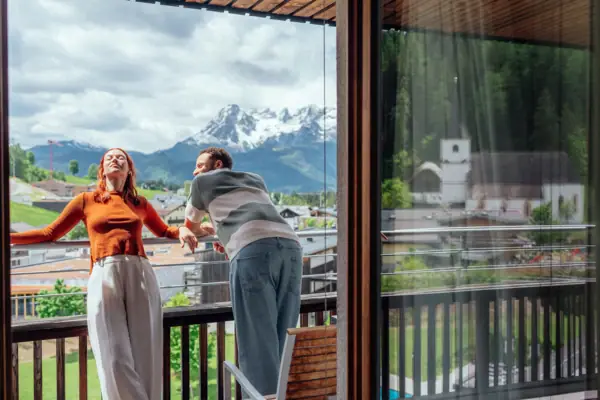 A man and a woman are standing on a veranda, looking out at the mountains.
