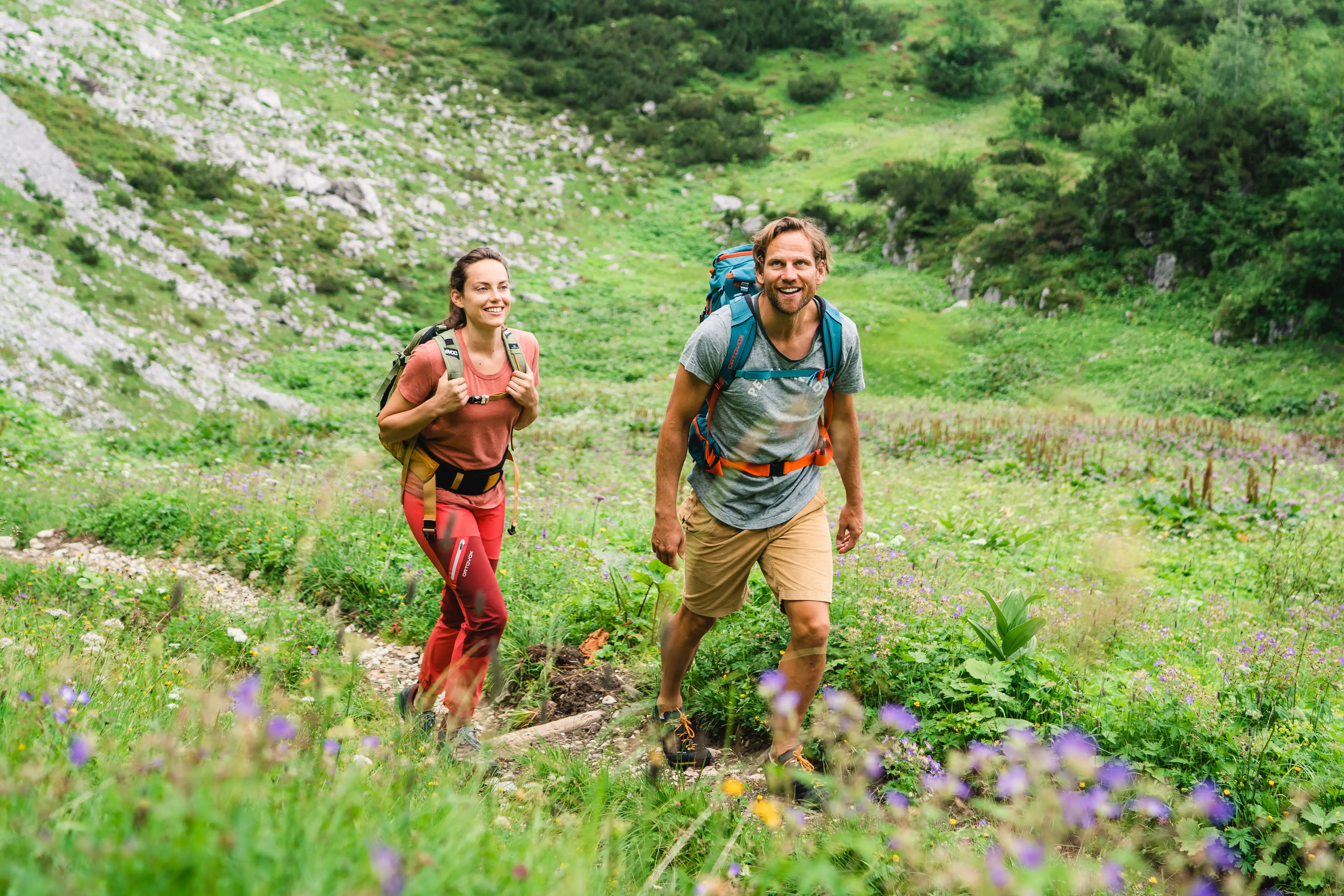 A woman and a man hike along a small path through a mountain world.