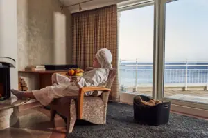 A woman in a white bathrobe sits in a chair with a bowl of fruit on her lap.