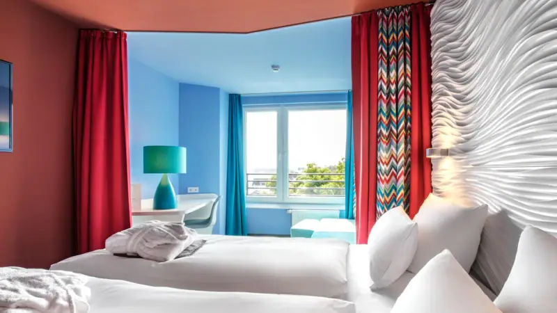 A room with two beds and red curtains.