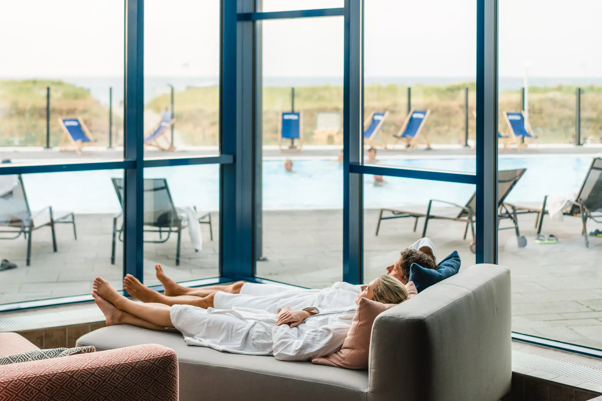 Rest and relaxation at aja Warnemünde A couple lie on a wellness sofa with a view of the outdoor pool.