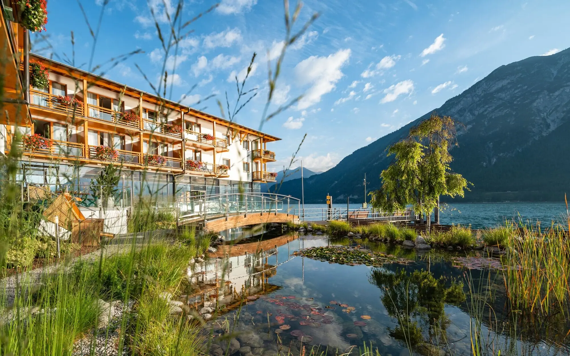 aja Fürstenhaus am Achensee next to the Achensee with a reflection of trees and clouds.