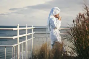 A woman in a bathrobe drinks from a cup.