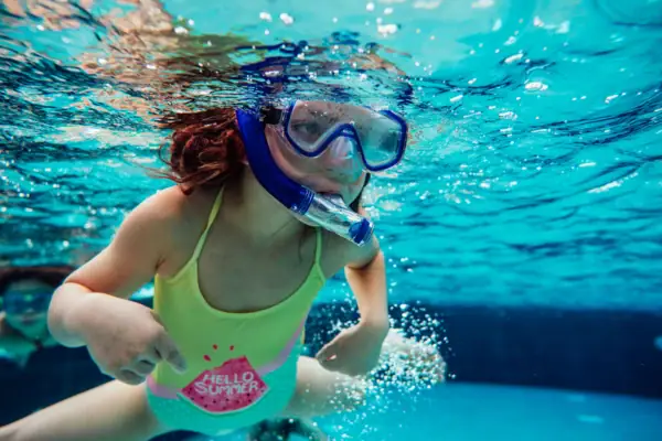 A girl with diving goggles snorkelling underwater.
