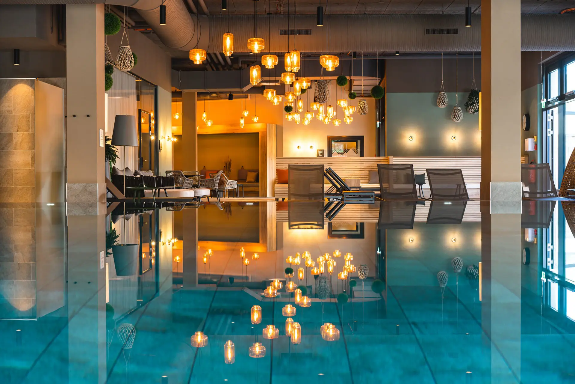 A modern indoor pool area with sun loungers and lamps in the background.