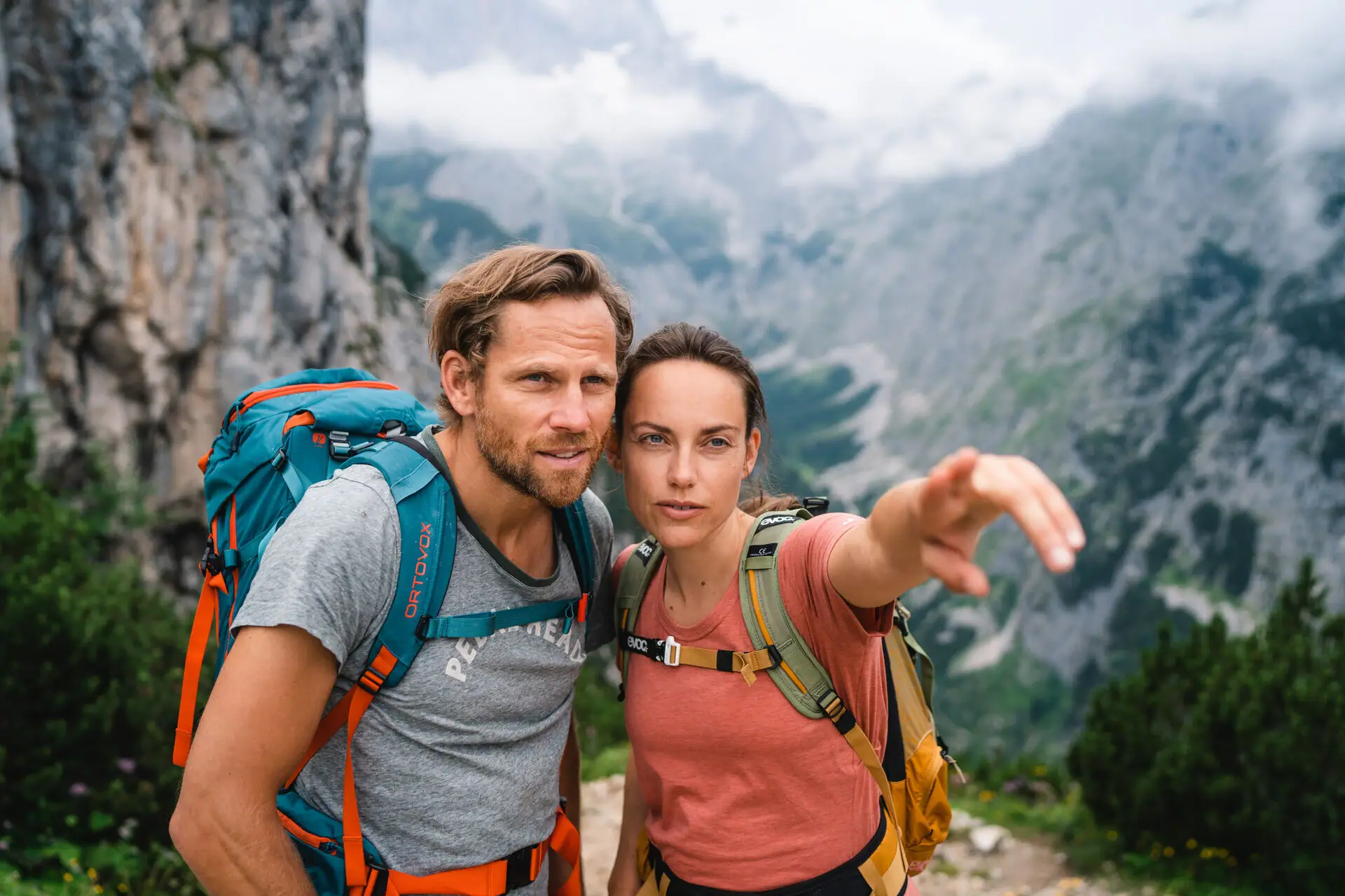 A man and a woman with rucksacks are standing on a mountain.
