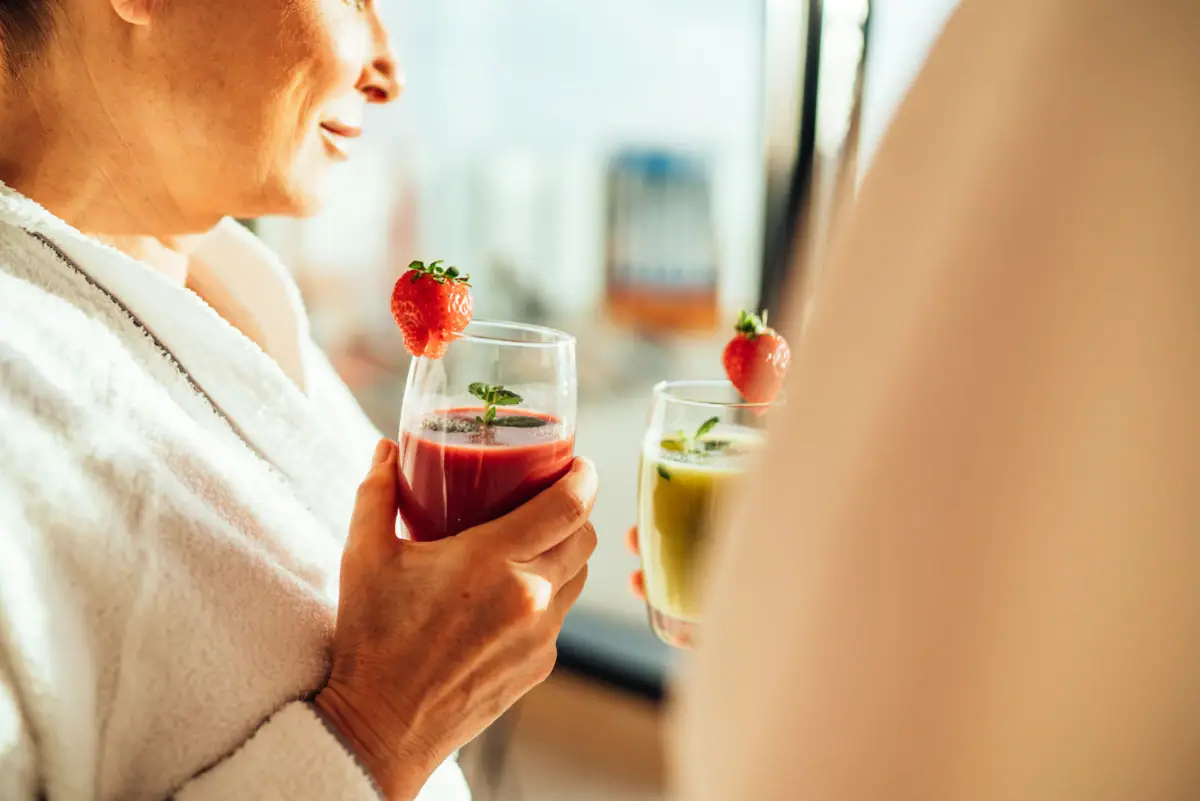 Woman in bathrobe holding drinks.
