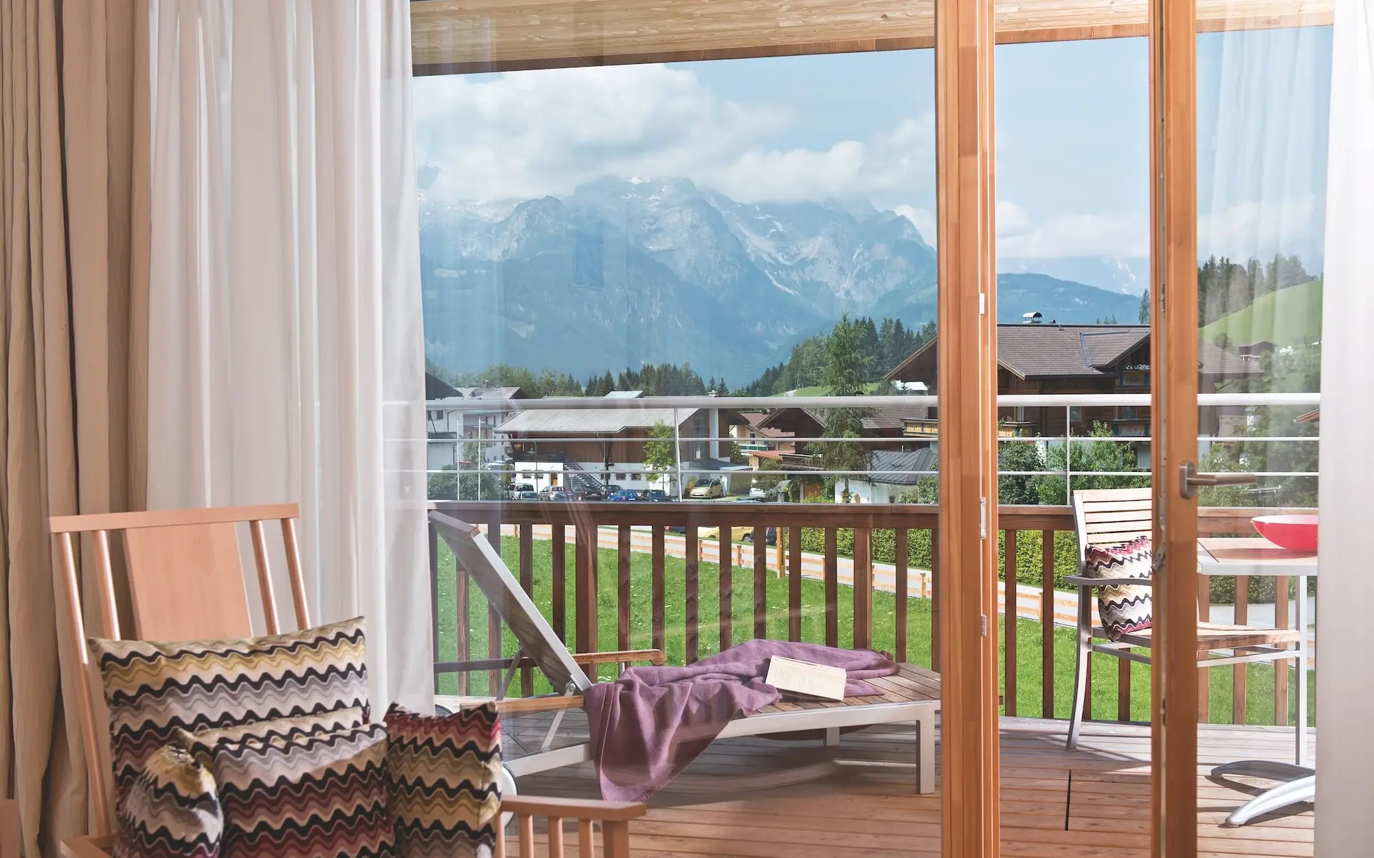 Balcony with view of mountains and trees, furnished with table and chairs.