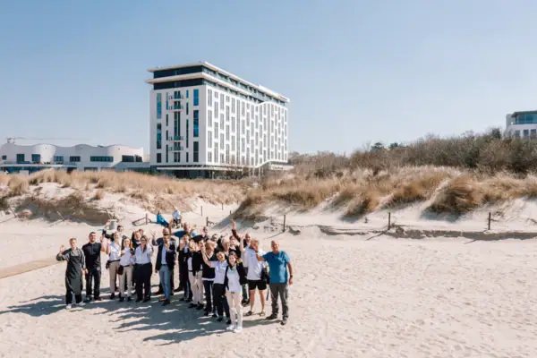 A group of people from the hotel team pose for a photo in front of the aja Warnemünde building.