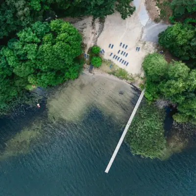 A footbridge over a body of water with chairs and trees.