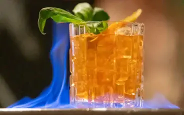 A cocktail in an old fashioned glass with ice cubes that is on fire.