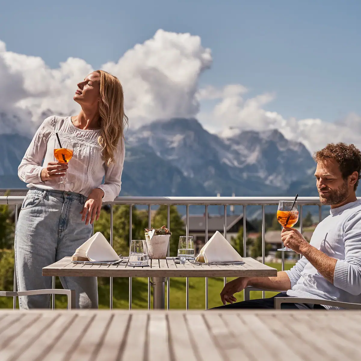 A man and a woman drink from a glass on a balcony.
