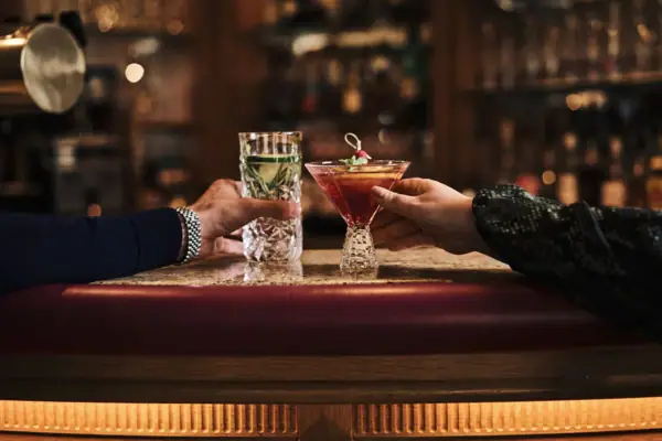 Two hands holding drinks on a bar counter.