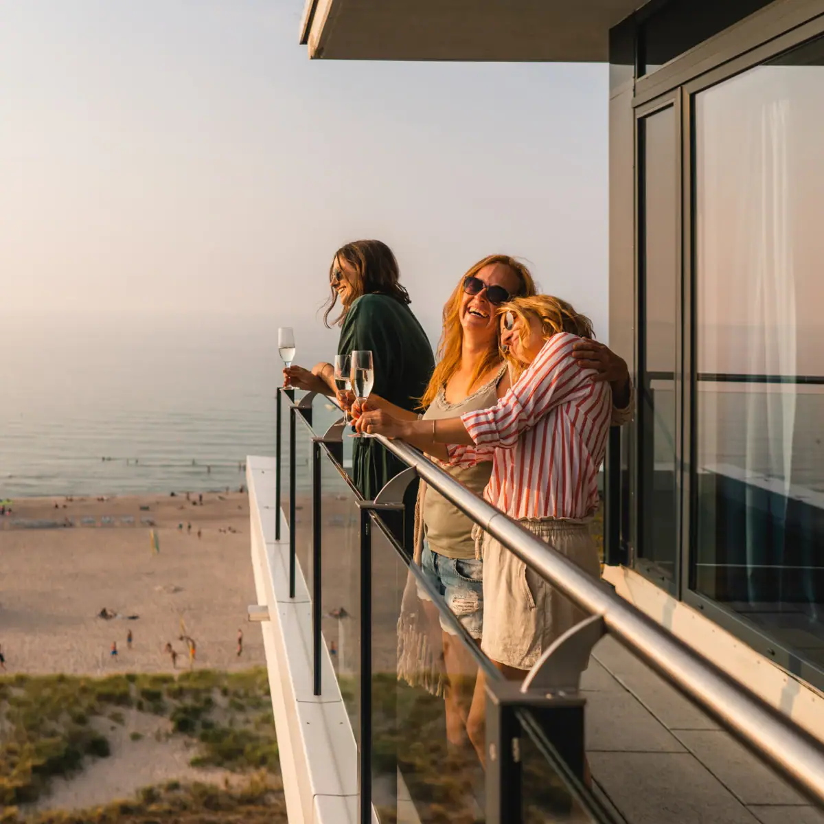 Balcony at aja Warnemünde A group of women stand on a balcony overlooking the beach.