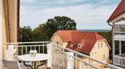 Balcony with table in front of a house surrounded by trees.