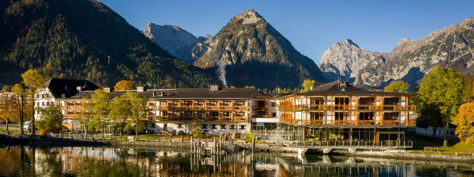A building next to a lake with a mountain in the background and trees reflecting on the water.