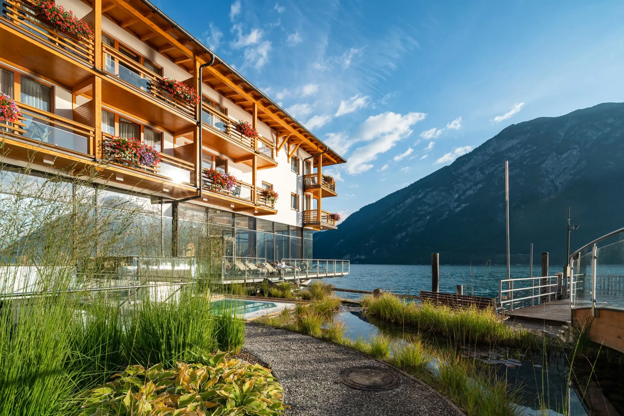 A building with a lake and mountains in the background under a partly cloudy sky.