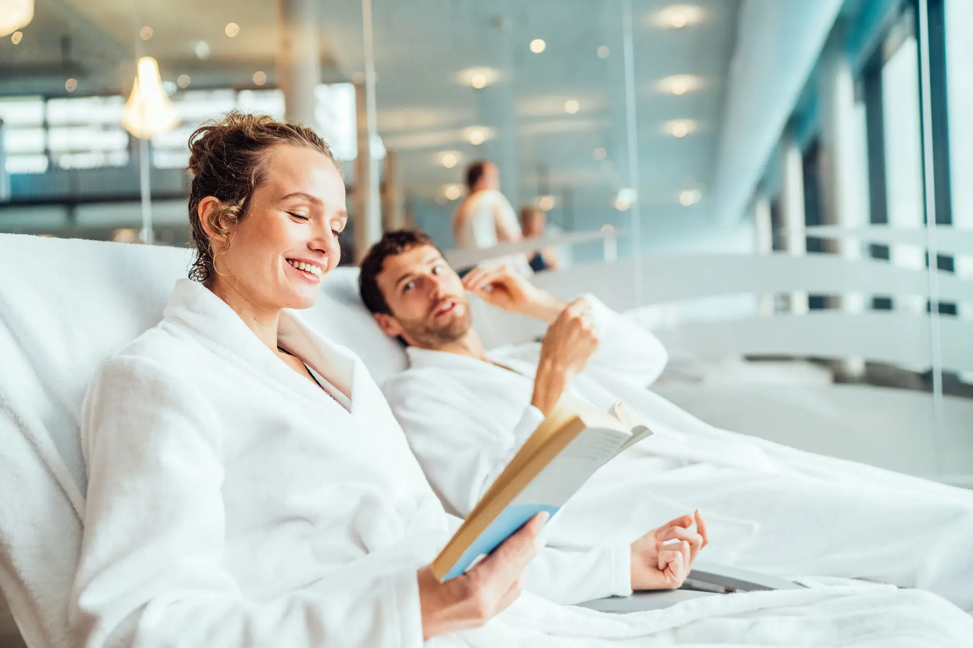 A man and a woman in bathrobes are reading a book.