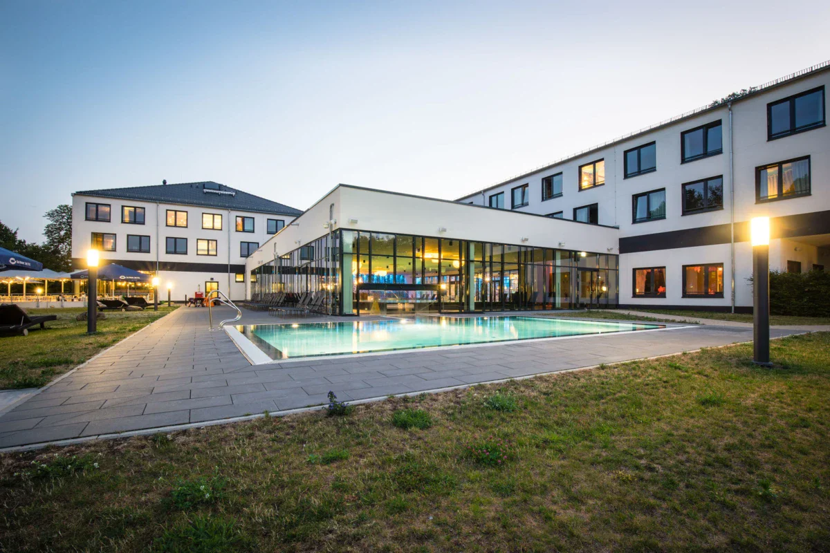 aja Bad Saarow A hotel building with a swimming pool and lawn.