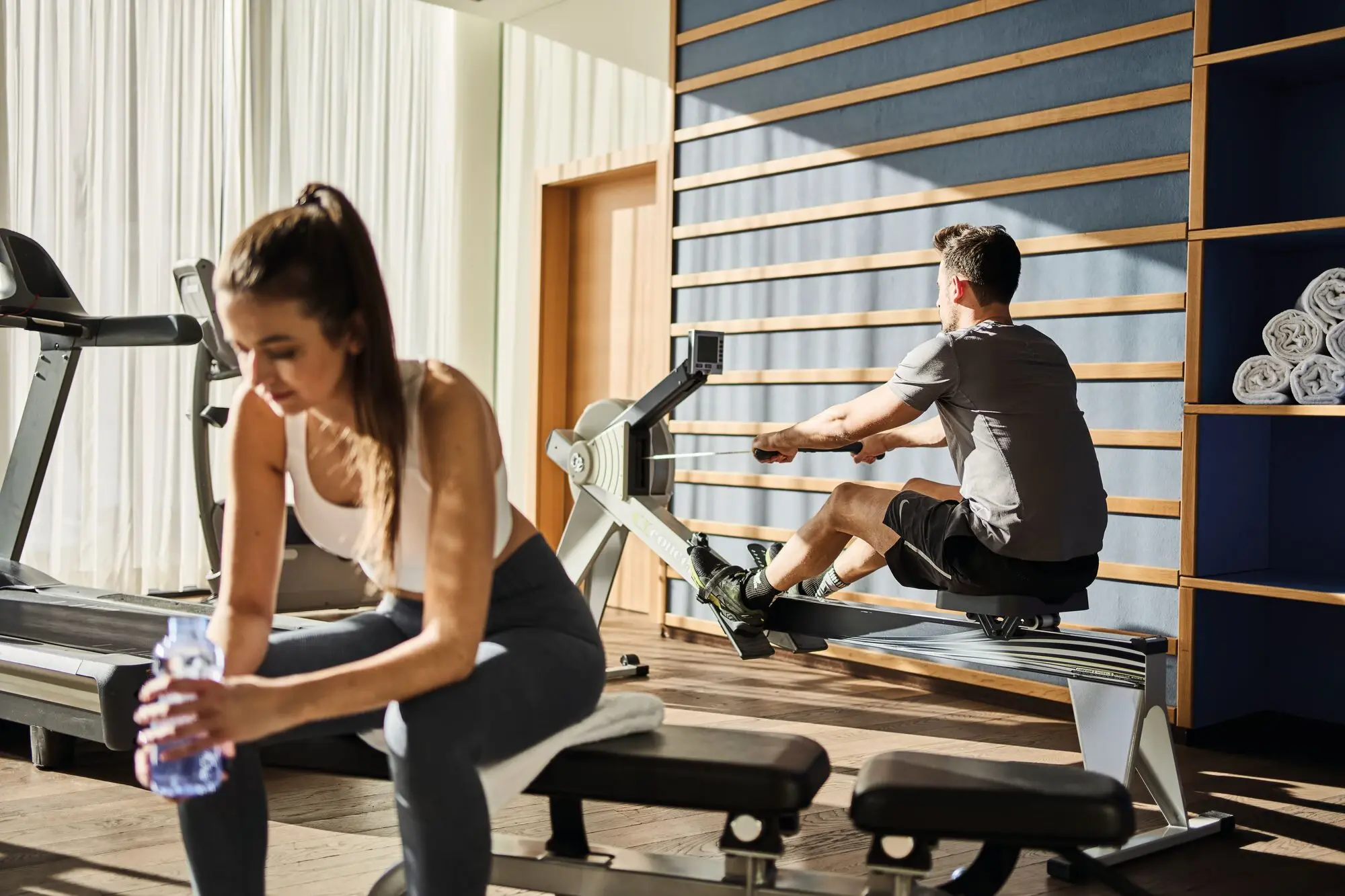 A man and a woman work out on fitness equipment in a gym.