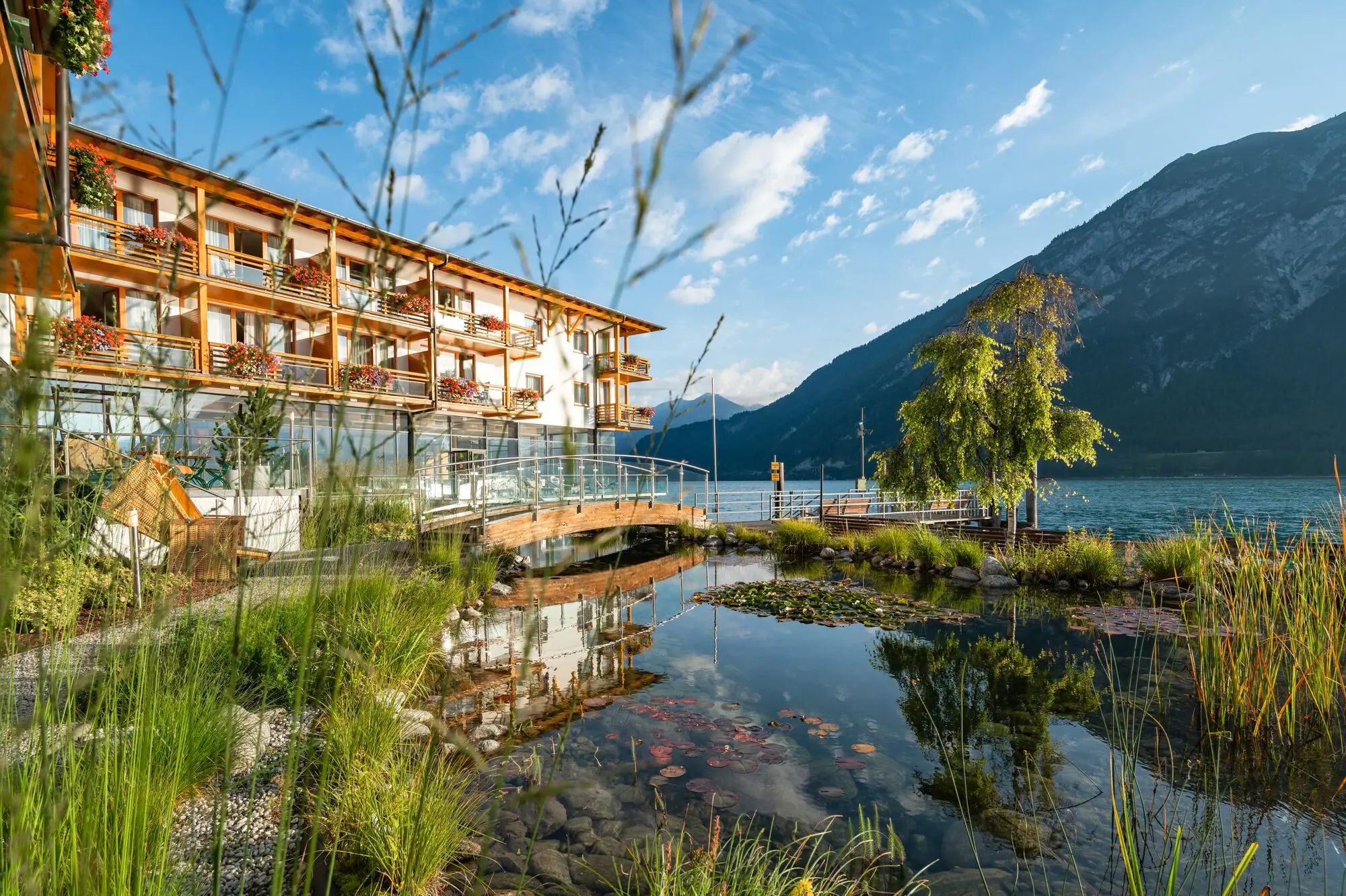 aja Fürstenhaus am Achensee Ein Gebäude neben einem Gewässer mit Bäumen und Wolken im Hintergrund.