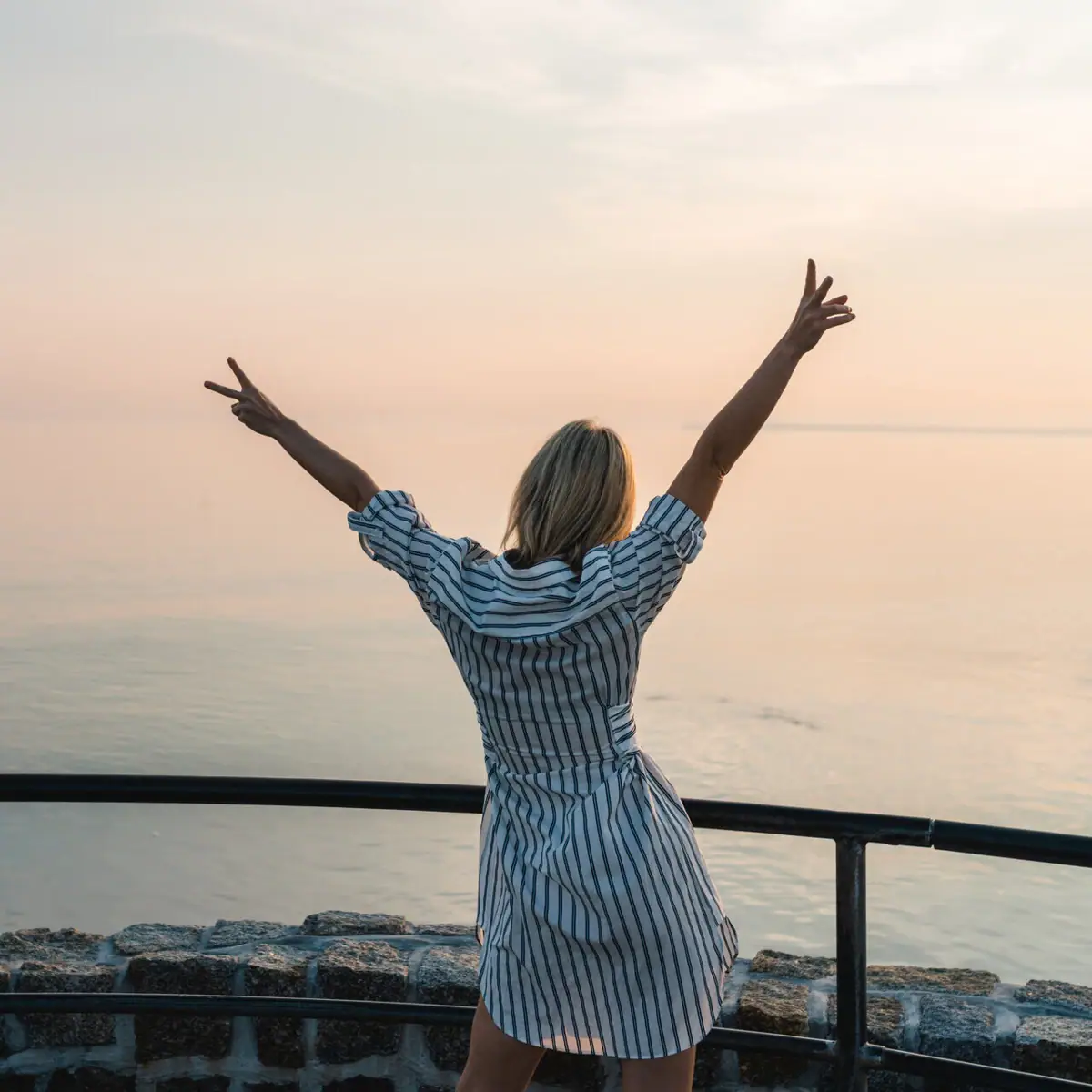 A woman sits on a railing with her arms raised.