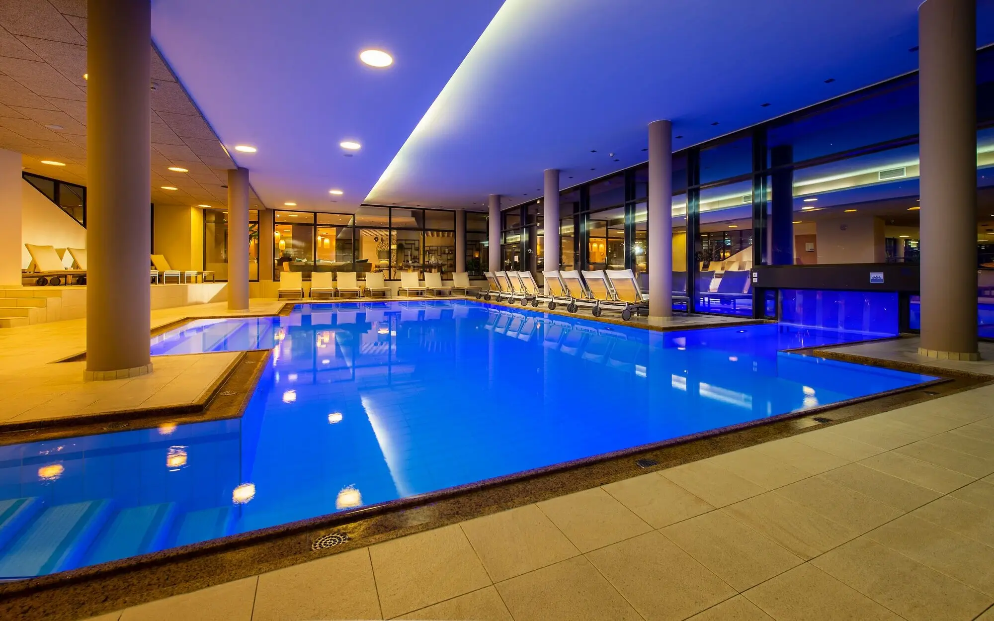 Indoor pool in a building at night, with blue water.