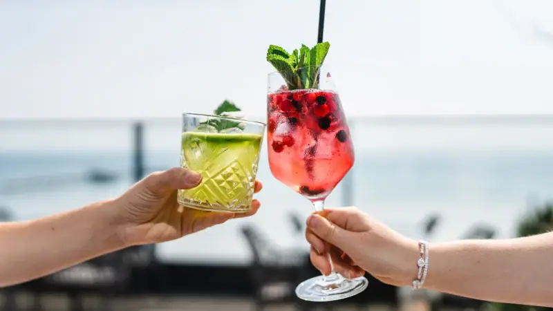 A pair of hands holding cocktails with strawberry garnish.