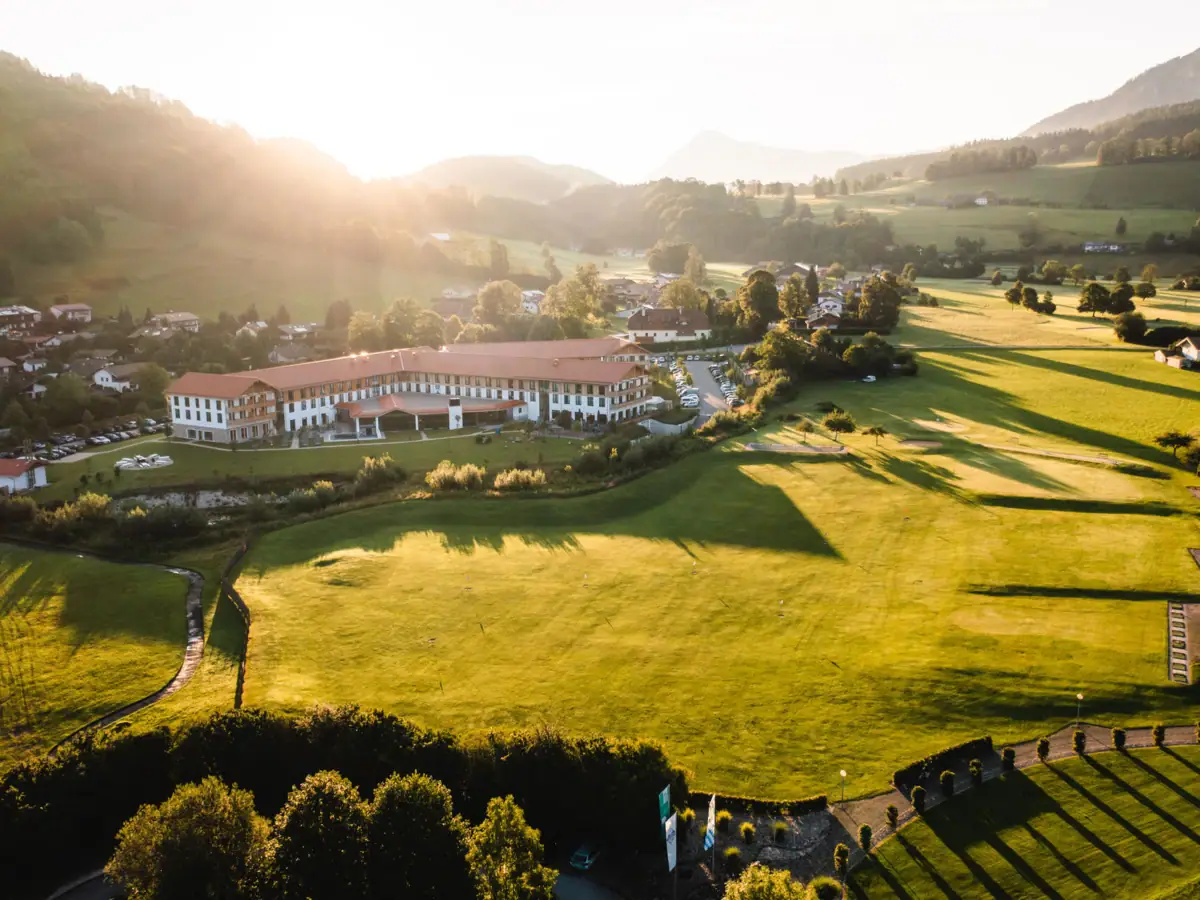 Green field with a building and trees in the background.