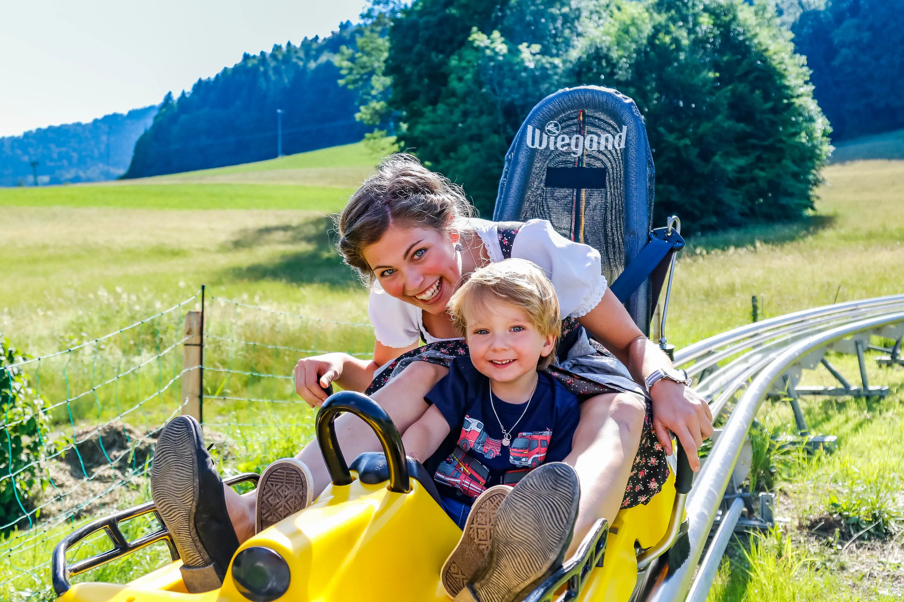 Chiemgau Coaster A woman and a small child on a sledge outdoors.