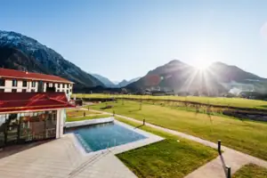Ein Swimmingpool in einer grasbewachsenen Fläche mit einem Gebäude und Bergen im Hintergrund.