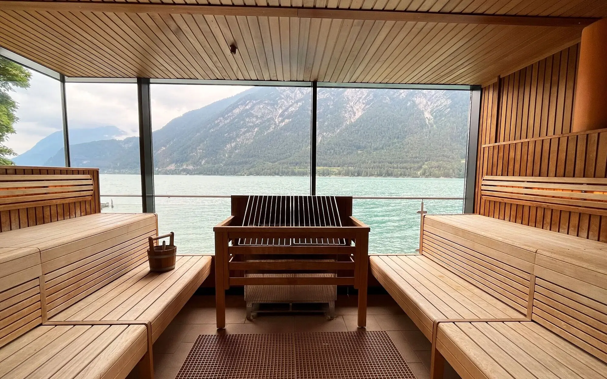 Large panoramic sauna with a view of the water and mountains, equipped with wooden benches.