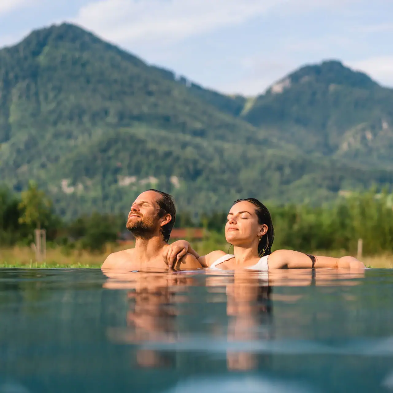 Day SPA in Ruhpolding A man and a woman in the pool with mountains in the background.