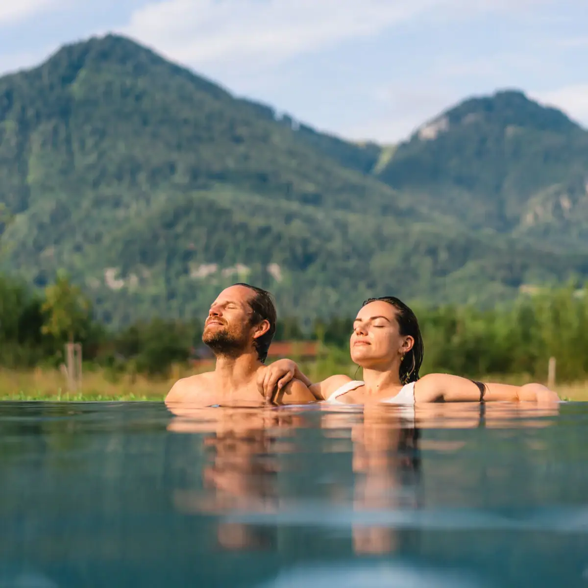 Outdoor pool at aja Ruhpolding A man and a woman in a pool with mountains in the background.