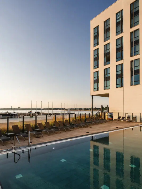 A pool with deckchairs and a building in the background.