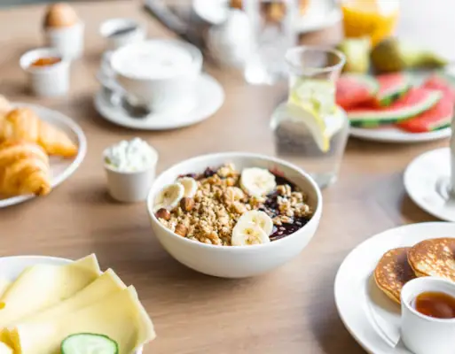Breakfast A bowl of muesli with bananas and pancakes on a table.