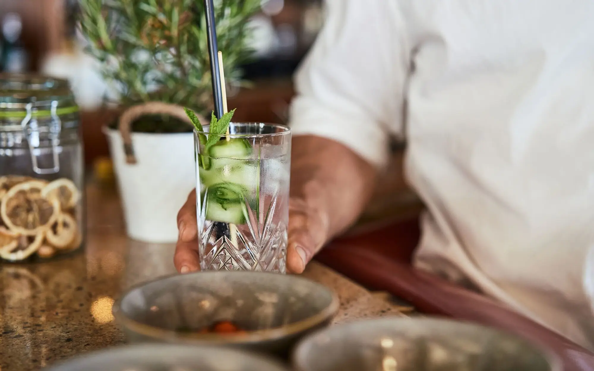 A man holds a long drink glass on a bar counter.