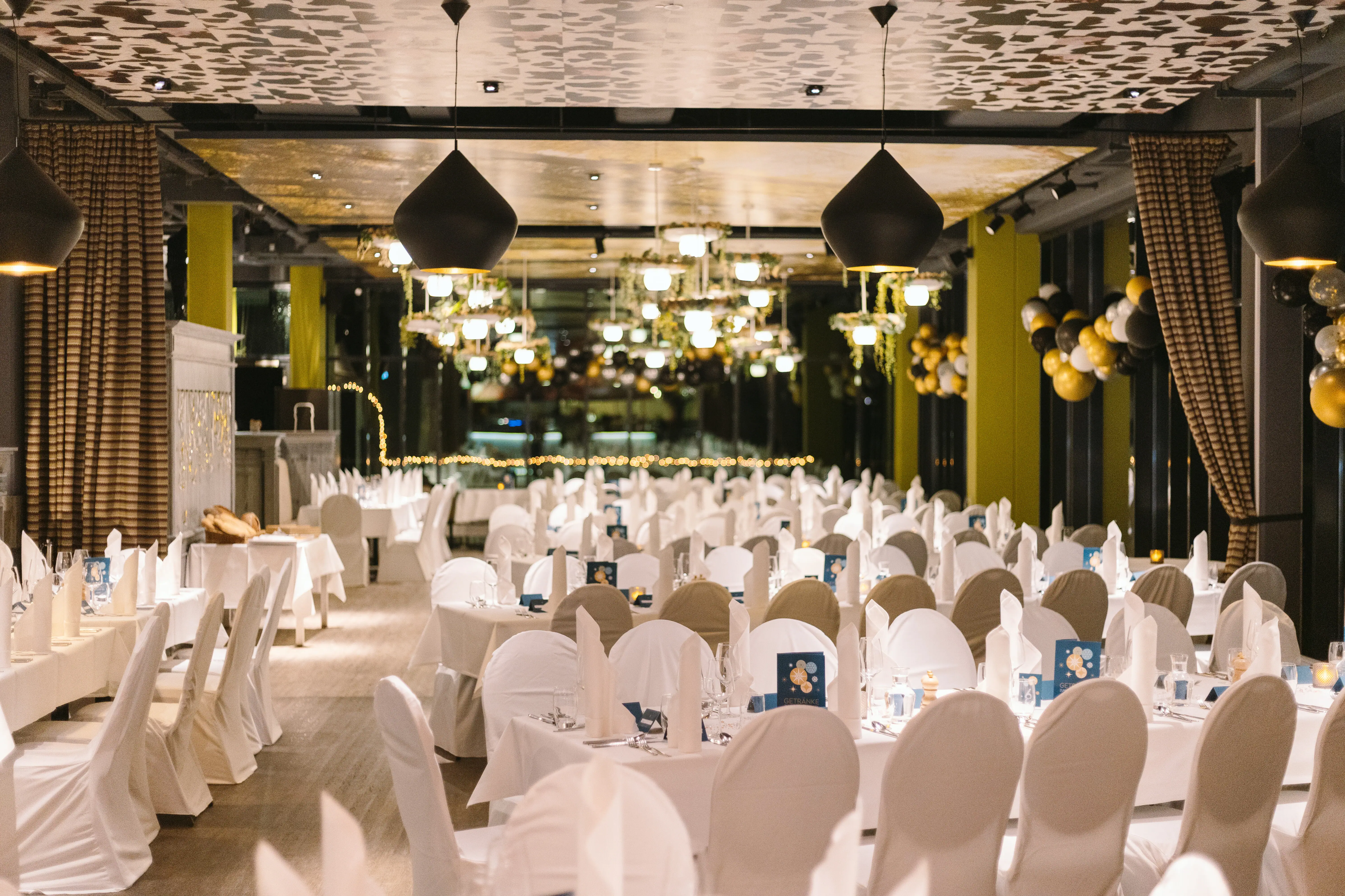 The restaurant at aja Bad Saarow is festively decorated. Various tables with white tablecloths and chair covers. 